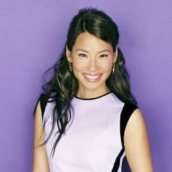 Lucy Liu in white dress smiling with a purple background drop