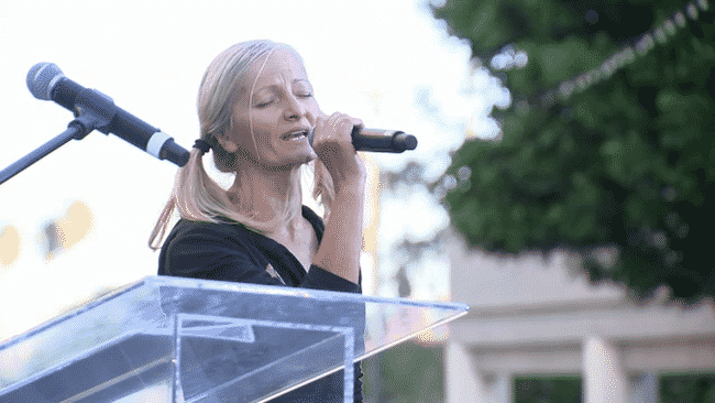 L.A. Subway Singer standing at podium with a mic in her hand