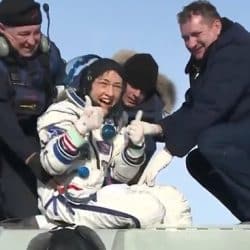 Chrsitina Koch touches down on earth wearing her spacesuit and smiling while two men help her balance