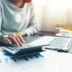 Close up hand of business woman using a calculator and a laptop