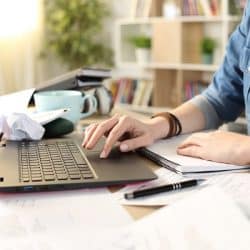 A woman's hands on a laptop, surrounded by clutter on a desk