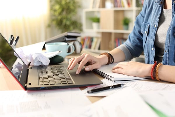 A woman's hands on a laptop, surrounded by clutter on a desk