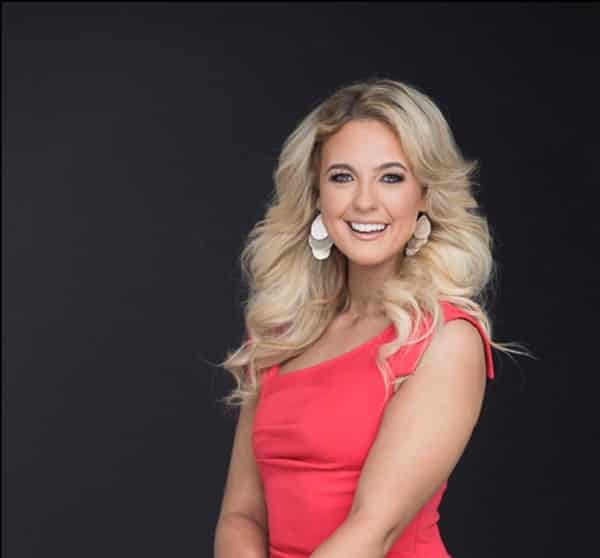 Madeline Delp, wearing a pink dress and smiling at the camera on a black cackground