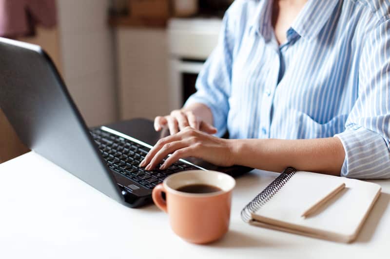 woman close up of hands on keyboard with cofeee and pen and paper on desk