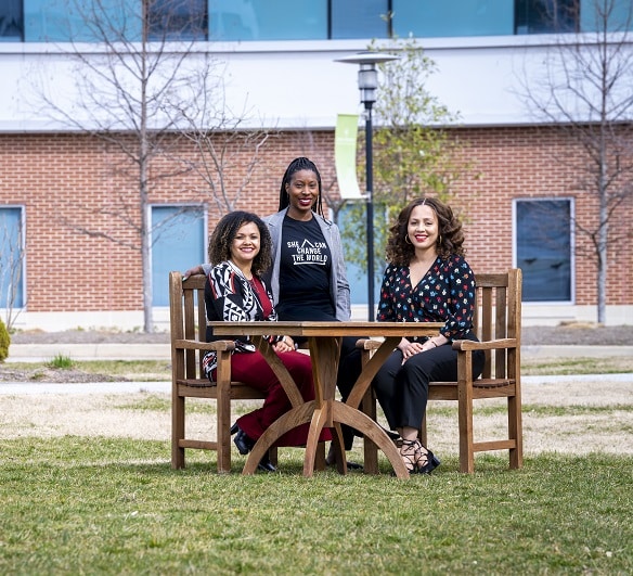 three black women nuclear engineers seated at table on the grass outside office building