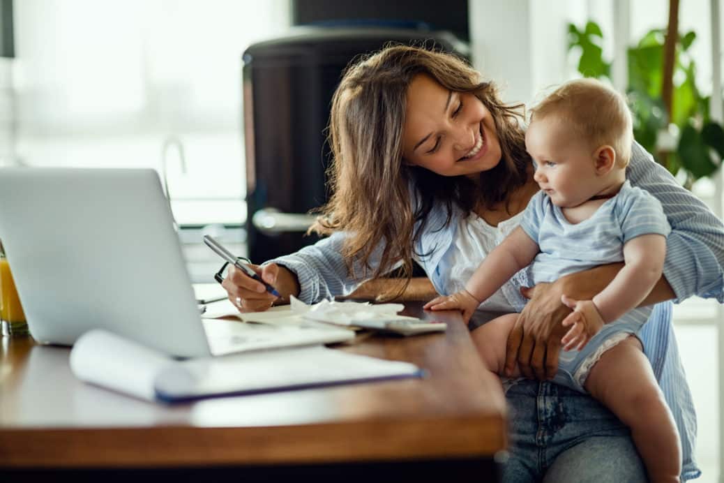 A woman holding her baby while working on a laptop