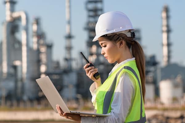 Woman on an energy industry site, looking at her laptop while wearing a hardhat