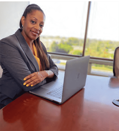 Mika Hilaire seaed at desk in professional attire with laptop open smiling