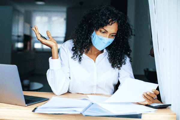 businesswoman-reviewing finances at desk with calculator and wearing a protective mask