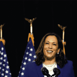 Vice President elect Kamala Harris stands behind podium smiling with U.S. flags int he background