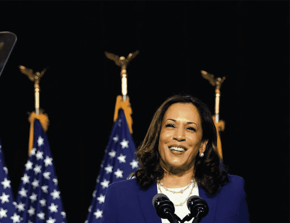 Vice President elect Kamala Harris stands behind podium smiling with U.S. flags int he background