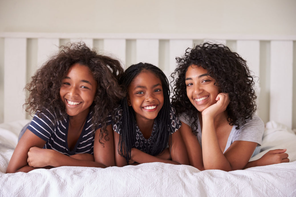 Three young girls lay on a bed laughing looking at the camera.