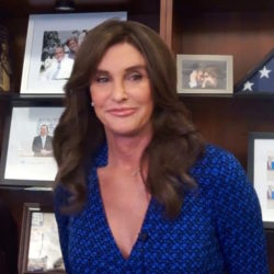 Cailtlyn Jenner in blue dress smiling in front of bookshelf with books and photos