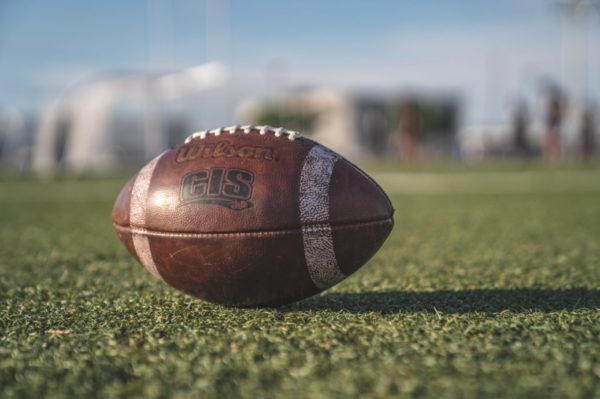 Football sitting in the middle of a grass field with an unfocused city skyline behind it