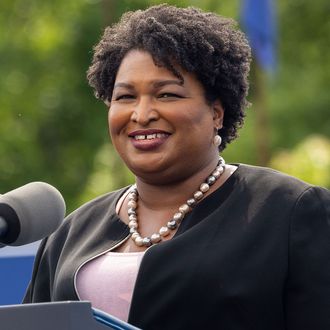 Stacey Abrams standing in front of a microphone stand while smiling away from the camera.