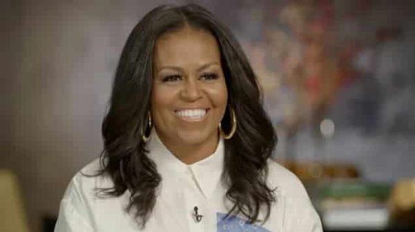 Michelle Obama smiling at the camera while wearing a white button up