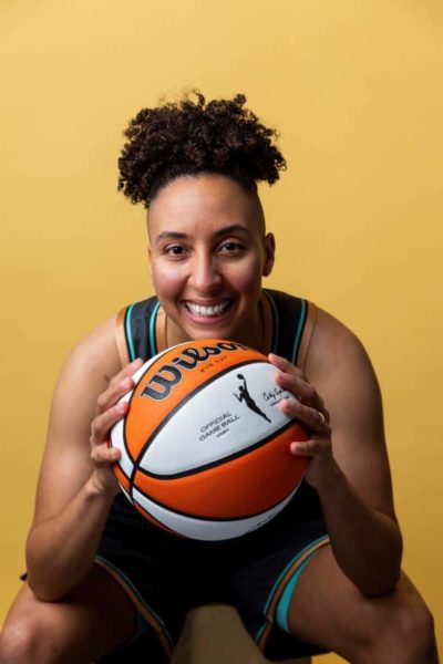 Trans athlete for the WBNA posing for a portrait image while holding a basketball up to the camera smiling