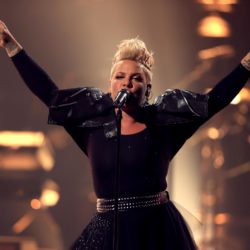 pink on stage singing with both arms up in the air