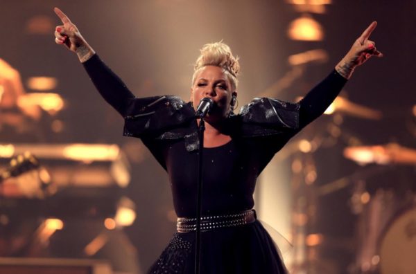 pink on stage singing with both arms up in the air