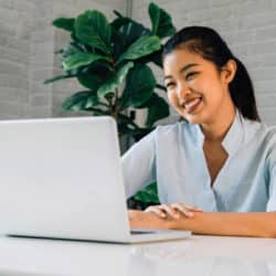 smiling asian woman on her laptop seated at a desk