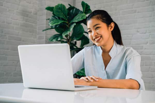 smiling asian woman on her laptop seated at a desk