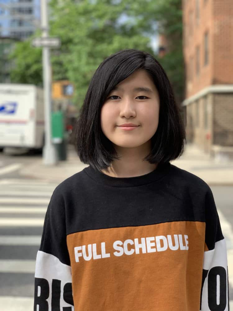 Emma Yang outdoors wearing a black and gold long sleeved sweater that says full schedule