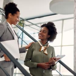 Happy black businesswoman talks to female mentor who leads her through office building