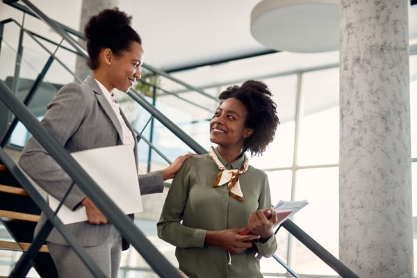 Happy black businesswoman talks to female mentor who leads her through office building