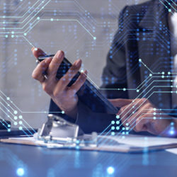 Businesswoman at desk checking phone with tech graphs in background