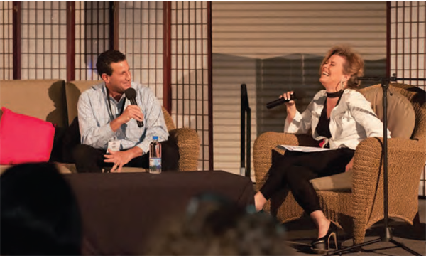 honna Jordan onstage sitting on couch talking to male guest laughing
