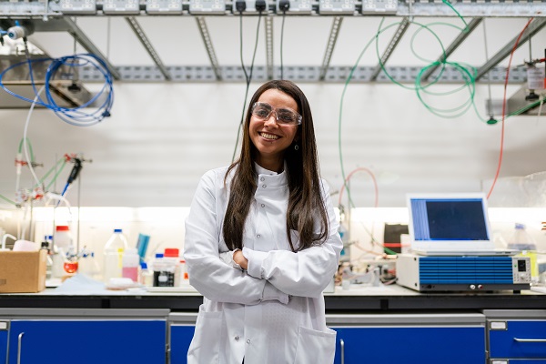 young Hispanic woman in lab coat with technology equipment behind her