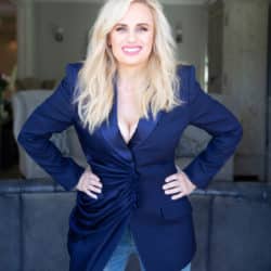 Rebel Wilson wearing a blue velvet blazer while smiling at the camera