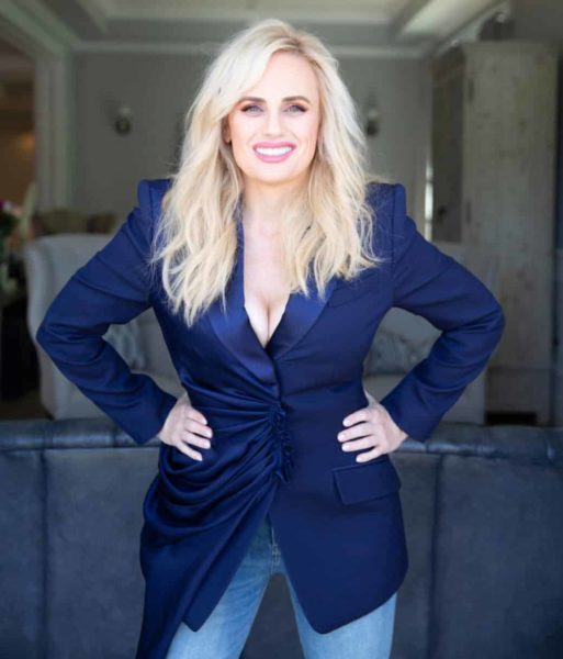 Rebel Wilson wearing a blue velvet blazer while smiling at the camera