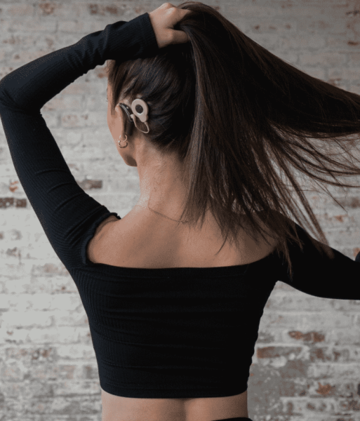 Abigail Heringer with her back facing the camera as she lifts her hair to show her new cochlear implant