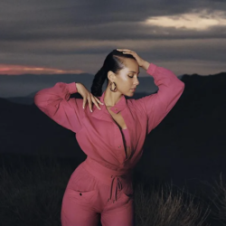 Alicia Keys wearing a pink jumpsuit during sunset posed to the side with one hand over her head and one on her own shoulder