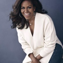 Michelle Obama Smiling at the camera in a white sweater and blue jean pants