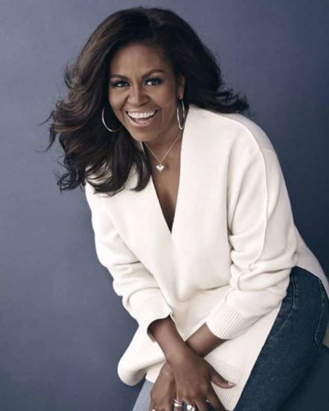Michelle Obama Smiling at the camera in a white sweater and blue jean pants