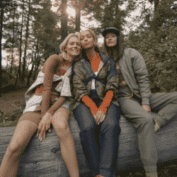 Three women sitting on a tree stump in the outdoors