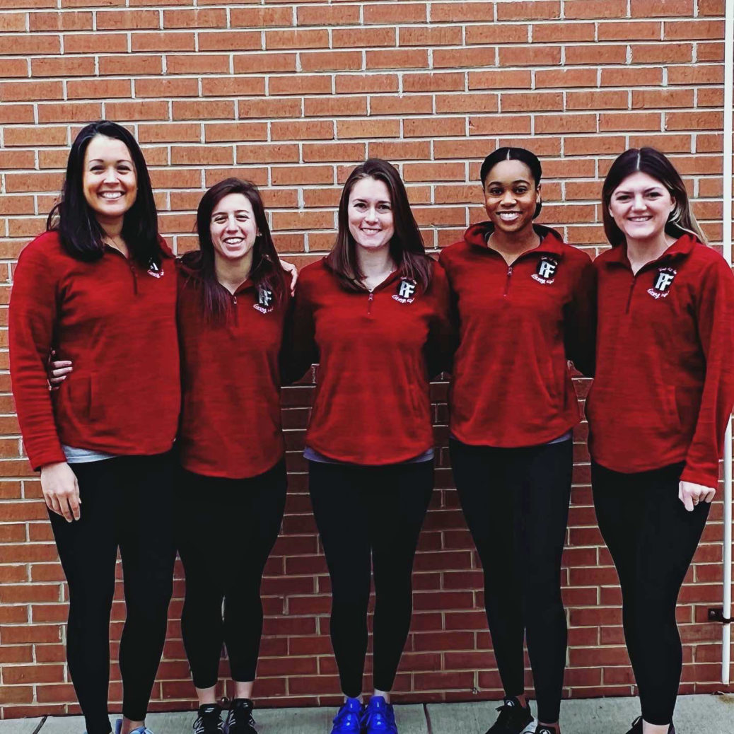 group of five women lined up against brick background wearing fitness clothes