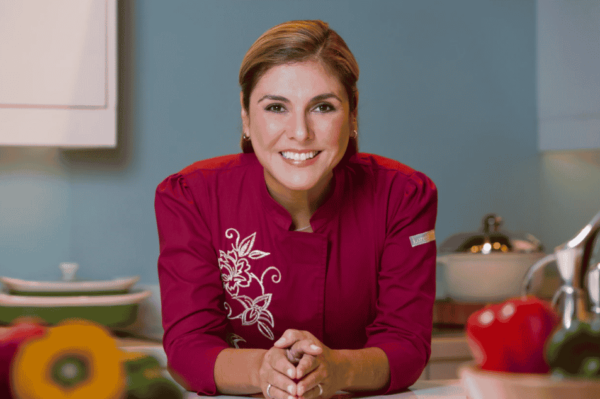 Renowned Latina chef Lorena Garcia wearing a red chefs uniform while smiling at the camera