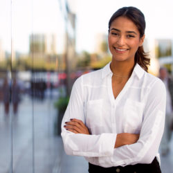 young female entrepreneur with arms folded smiling, blurred business background