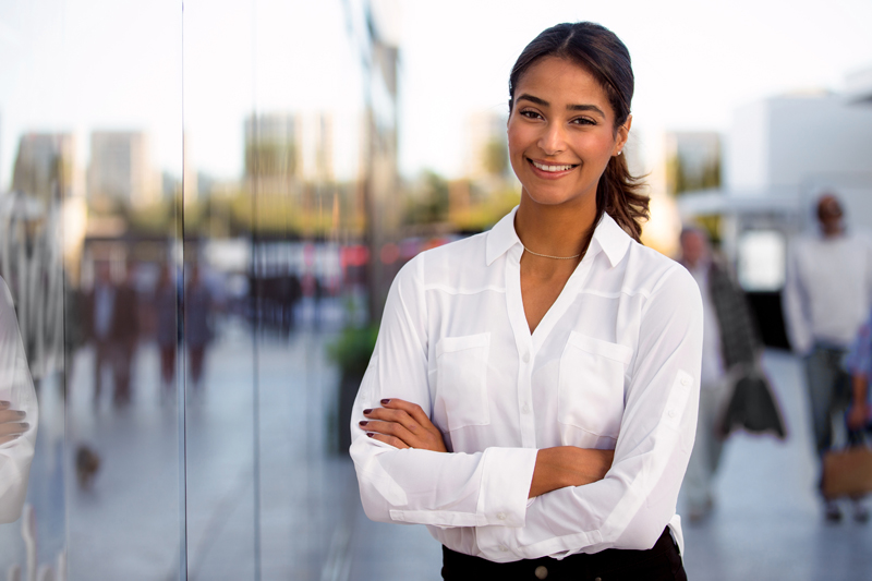 young female entrepreneur with arms folded smiling, blurred business background