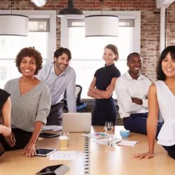 group of diverse career co-workers gathered around conference table with laptops