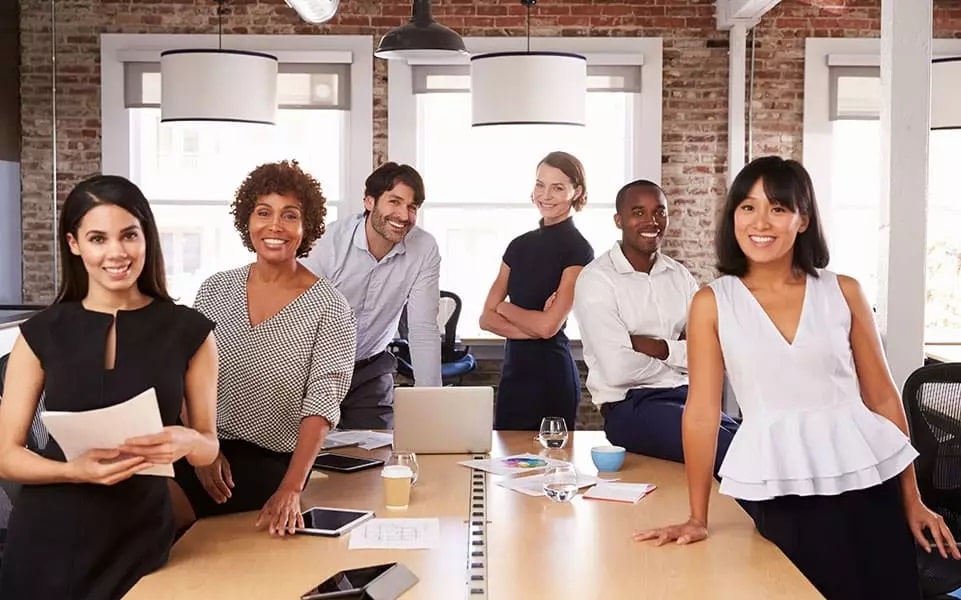 group of diverse career co-workers gathered around conference table with laptops